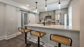 A modern kitchen with a central island, bar stools, stainless steel appliances, and pendant lighting.
