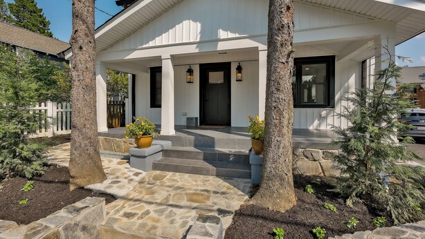 A white house with a stone pathway leading to the front door, surrounded by trees and potted plants.