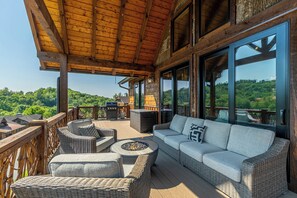 A covered outdoor seating area with wicker furniture, a fire pit, and a view of the surrounding landscape.