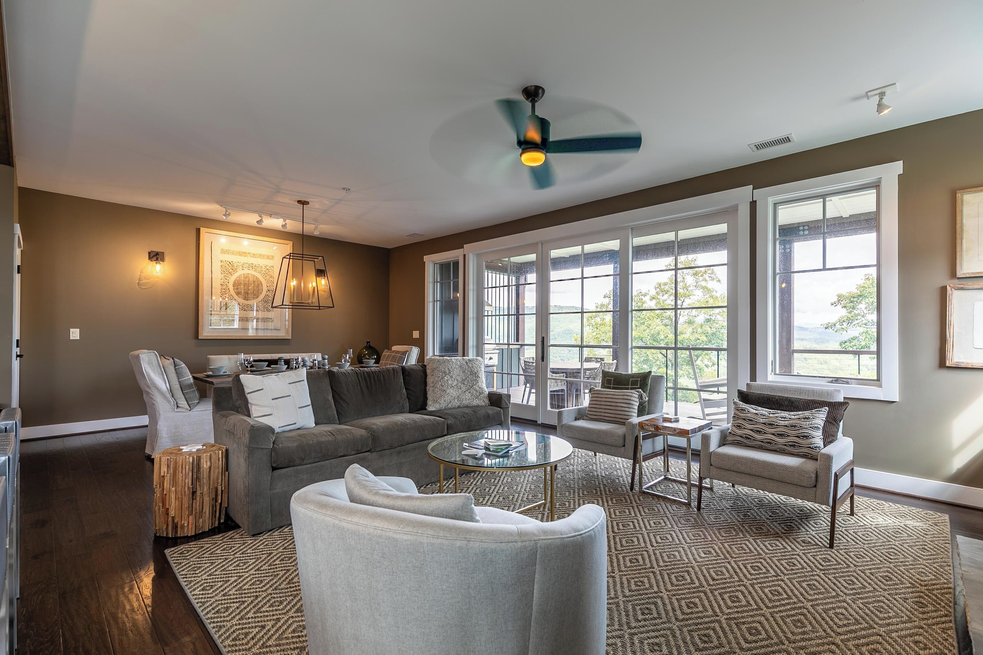 A spacious living room with a large window, a ceiling fan, and a modern fireplace.