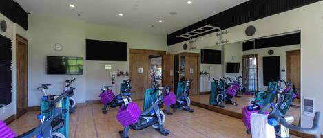 Un gimnasio con varias bicicletas estáticas, un banco y espejos en las paredes.