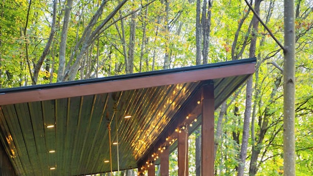 A covered outdoor seating area with wooden chairs and a barbecue grill, surrounded by trees. - Rekindled @ The Patch, lux couples getaway, hot tub, outdoor living. (Laurelville)