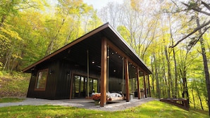 A modern cabin with a covered porch, large windows, and a swing chair. - Rekindled @ The Patch, lux couples getaway, hot tub, outdoor living. (Laurelville)