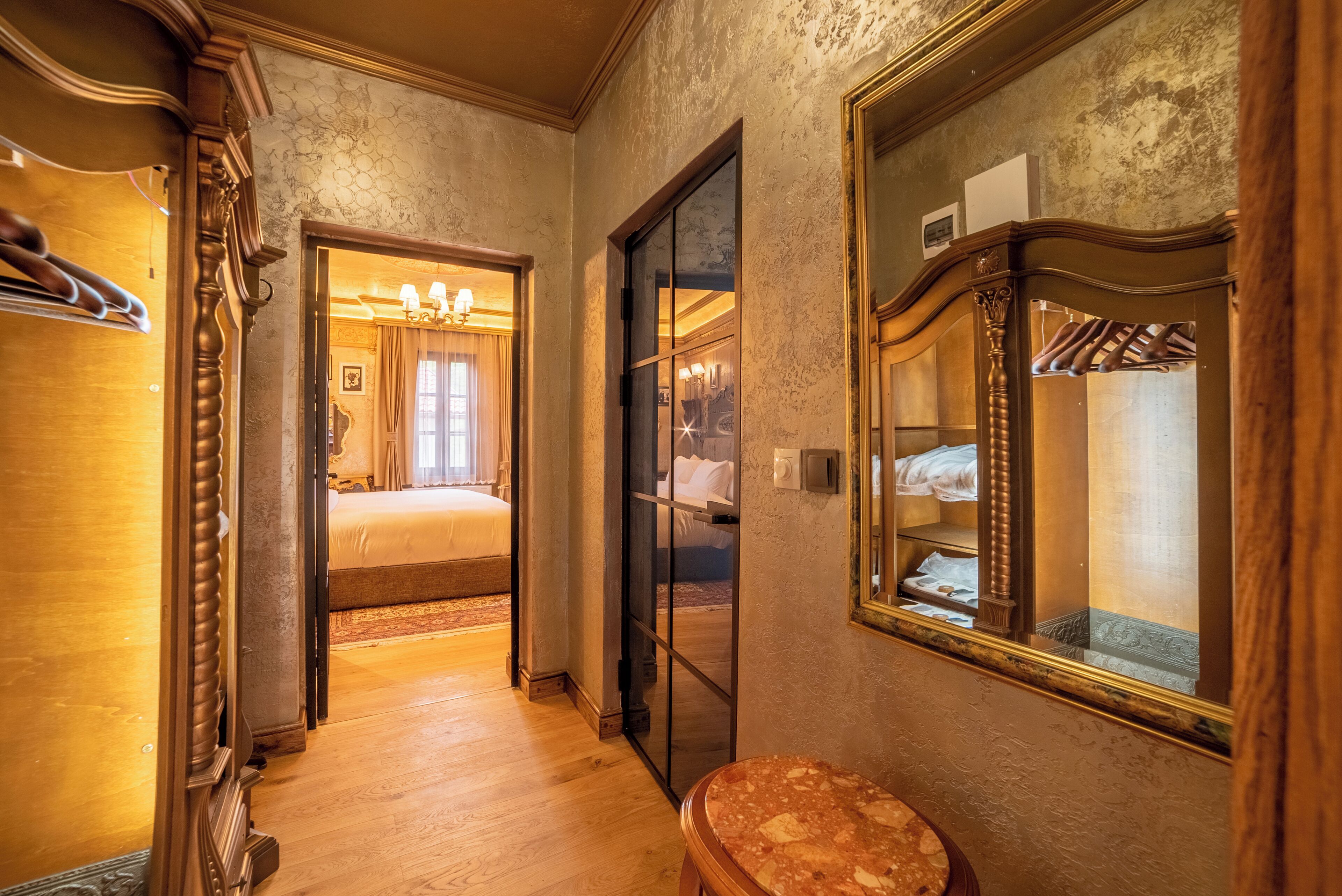 Habitació d'hotel amb sòl de fusta, un gran mirall, una banca de fusta i un llit amb capçalera blanca.