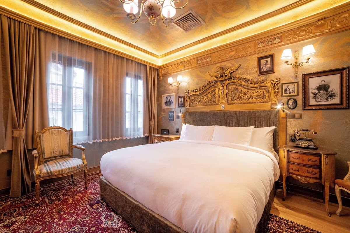 Ein großes Bett mit Holz Kopfteil, ein Sessel, ein Nachttisch mit Lampe und eine Wand mit gerahmten Bildern.