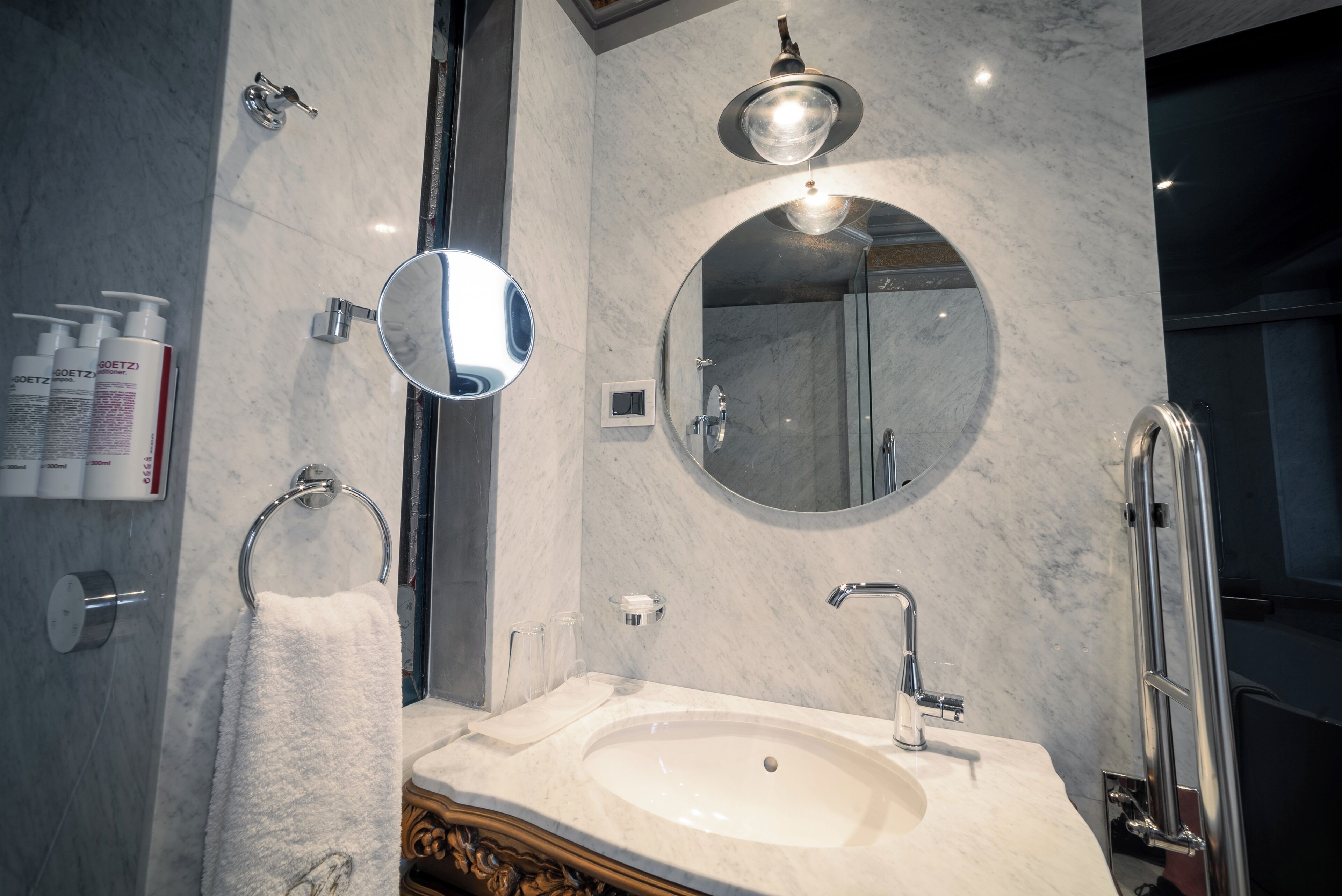 A modern bathroom with a marble sink, two mirrors, a towel ring, and a handheld showerhead.