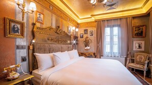 Een luxe hotelkamer met een groot bed, een gedetailleerd hoofdeinde en klassieke inrichting, waaronder ingelijste foto's en een vintage telefoon.