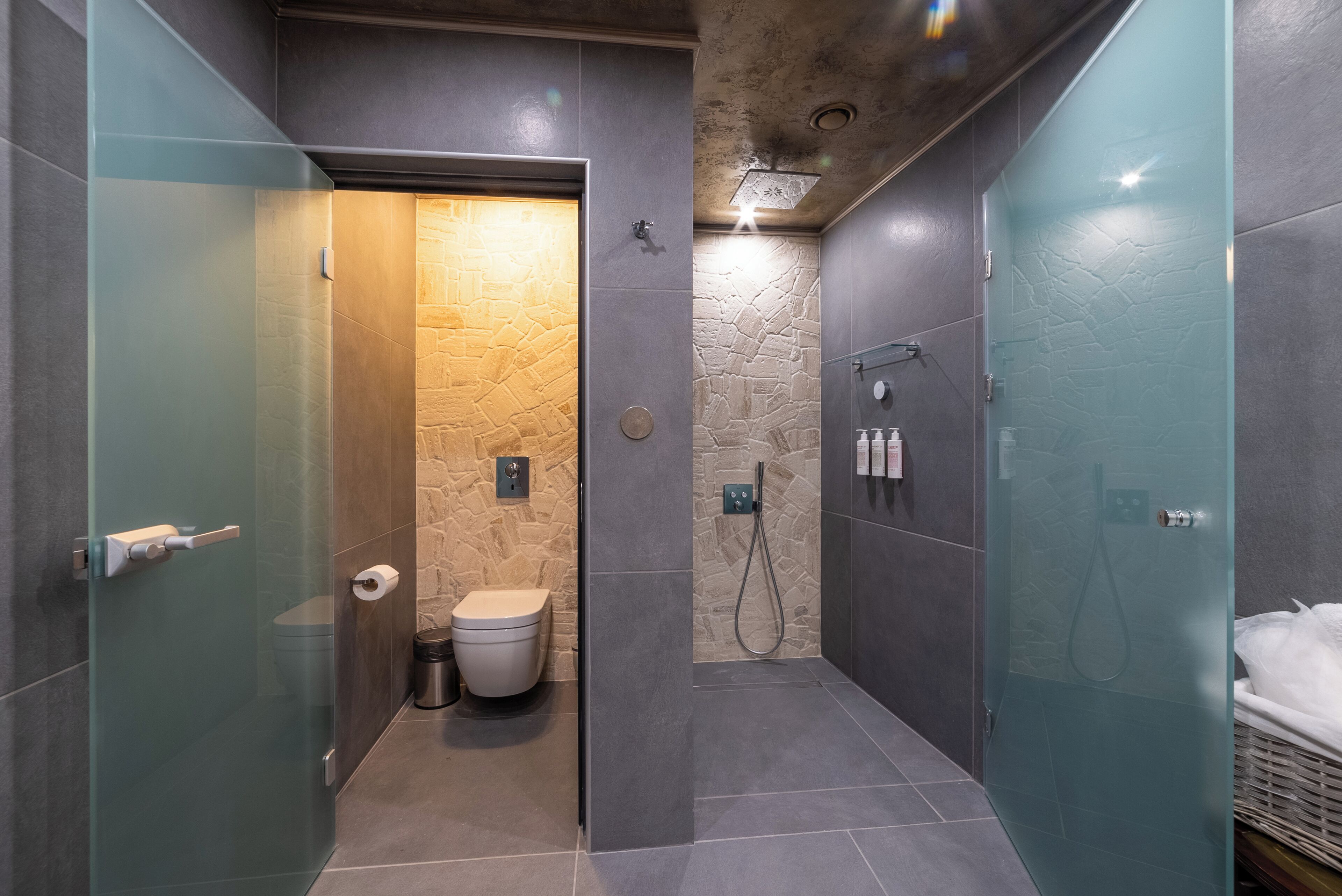 Une salle de bain moderne dotée d’une douche à parois de verre, d’un mur d’accent en pierre et d’un espace toilettes séparé.