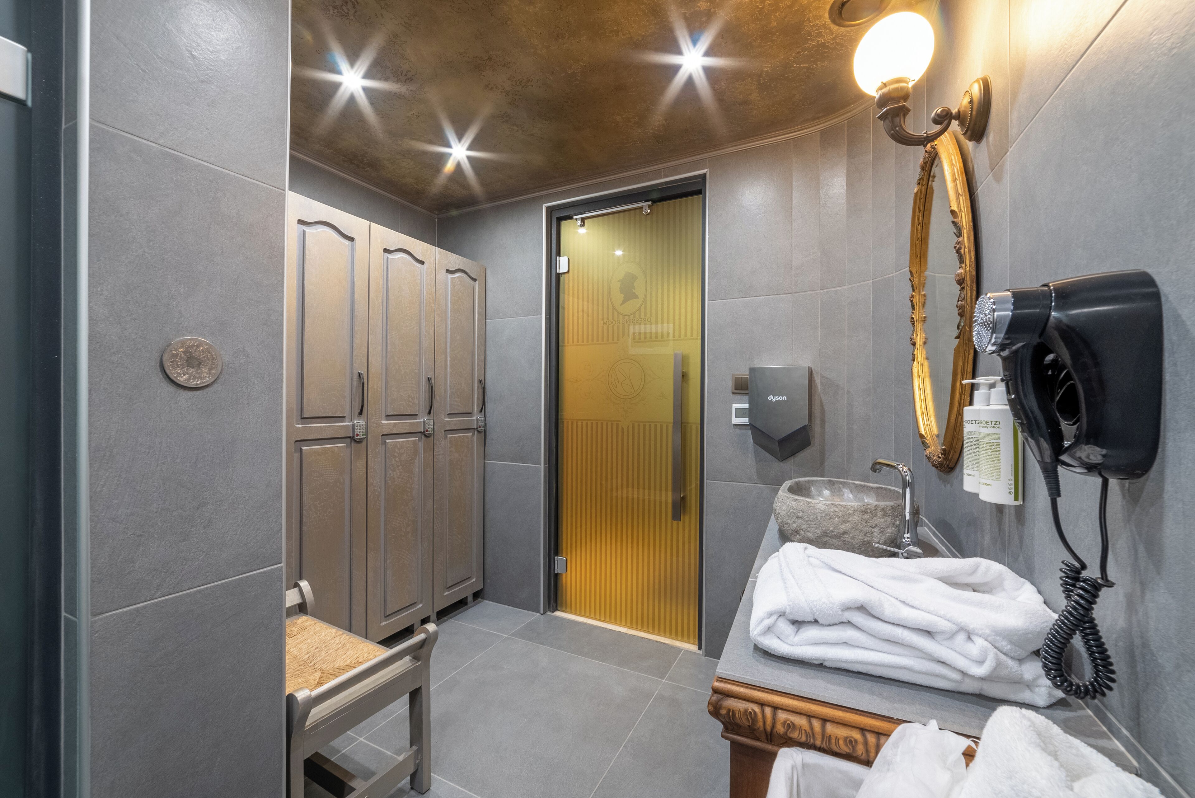 Un baño moderno con baldosas grises, un mueble de tocador de madera, un perchero para toallas y un secador de pelo.