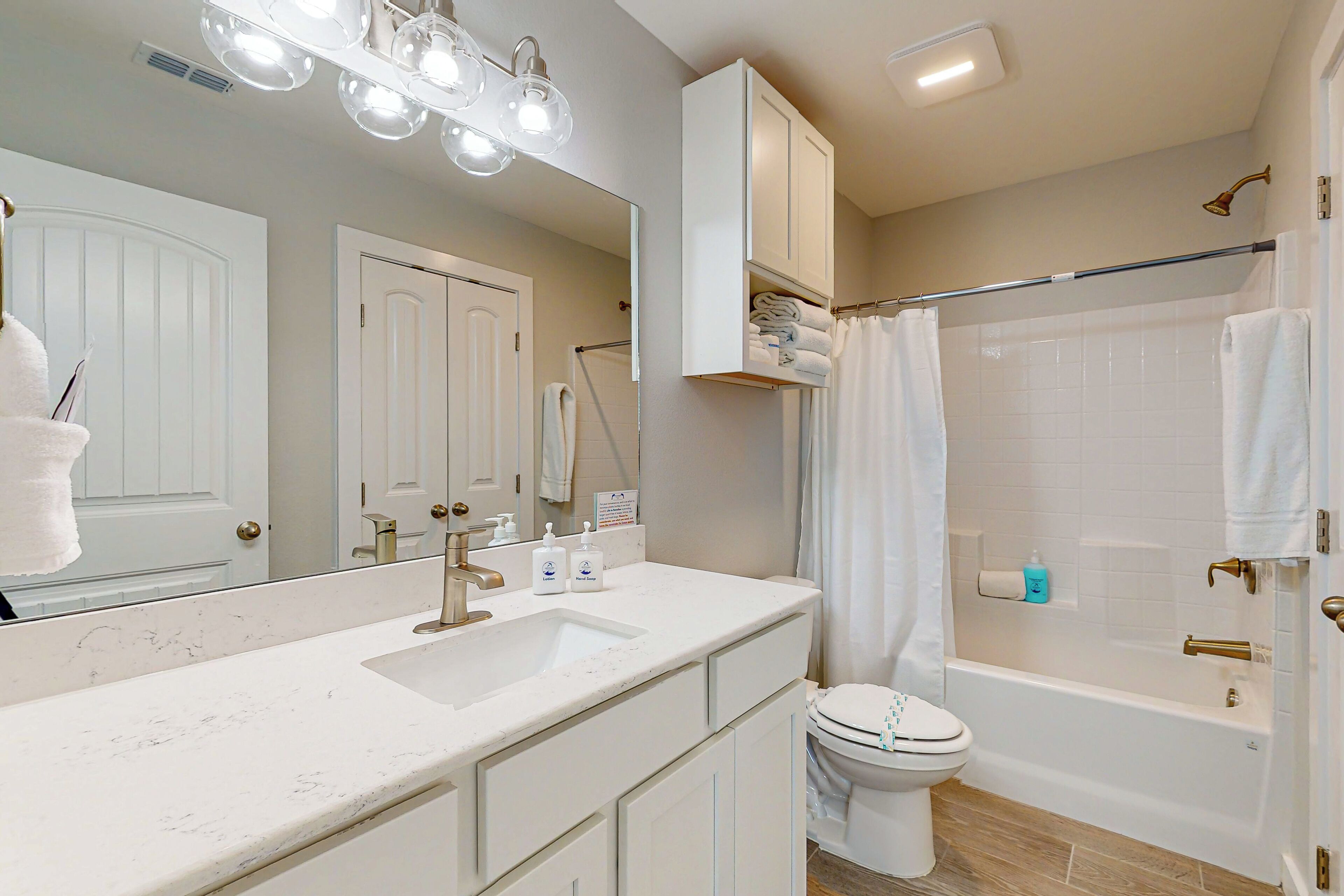 A modern bathroom with a large mirror, a sink with a vanity, a toilet, and a bathtub with a shower curtain.