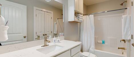A modern bathroom with a large mirror, a sink with a vanity, a toilet, and a bathtub with a shower curtain.