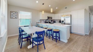 A modern kitchen with white cabinets, a central island with stools, and a dining table with chairs. - Private Heated Pool, Pet Friendly, Parking for 5 (Port Aransas)