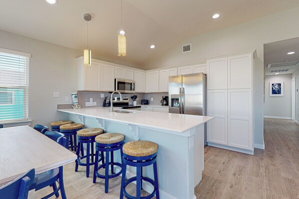 A modern kitchen with white cabinetry, a stainless steel refrigerator, a microwave, and a large island with bar stools.