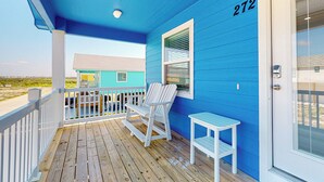 A blue house with the number 272, a porch with a white railing, a white chair, and a small table. - Private Heated Pool, Pet Friendly, Parking for 5 (Port Aransas)