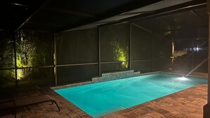 A swimming pool with a tiled deck, surrounded by a covered area with a roof.