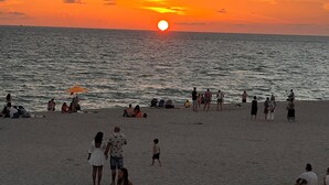 A beach scene with people relaxing and walking along the shore during sunset.