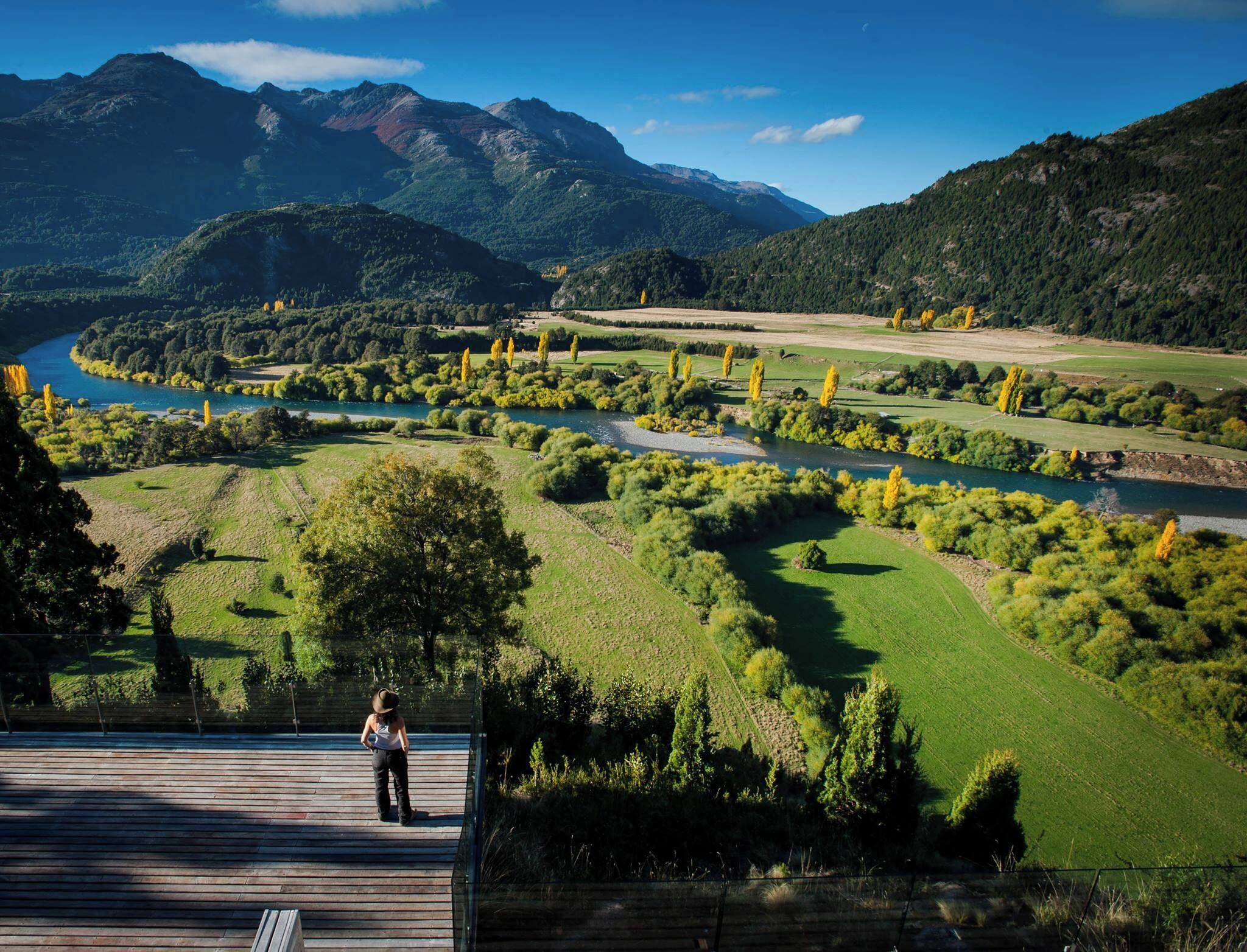 A scenic outdoor area with a wooden deck, a river, and mountains in the background.