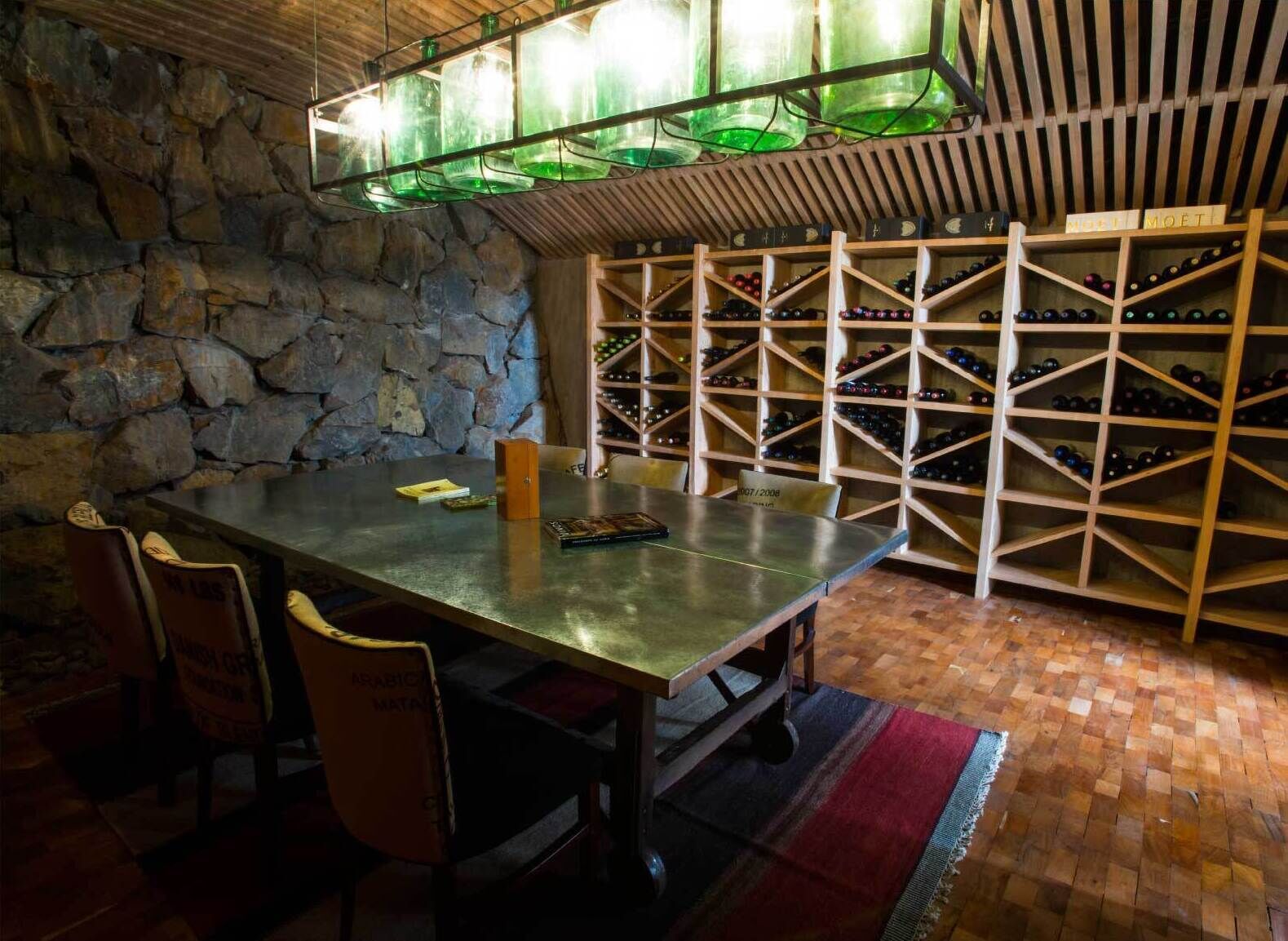 A wine cellar with a stone wall, wooden wine racks, and a table with chairs.