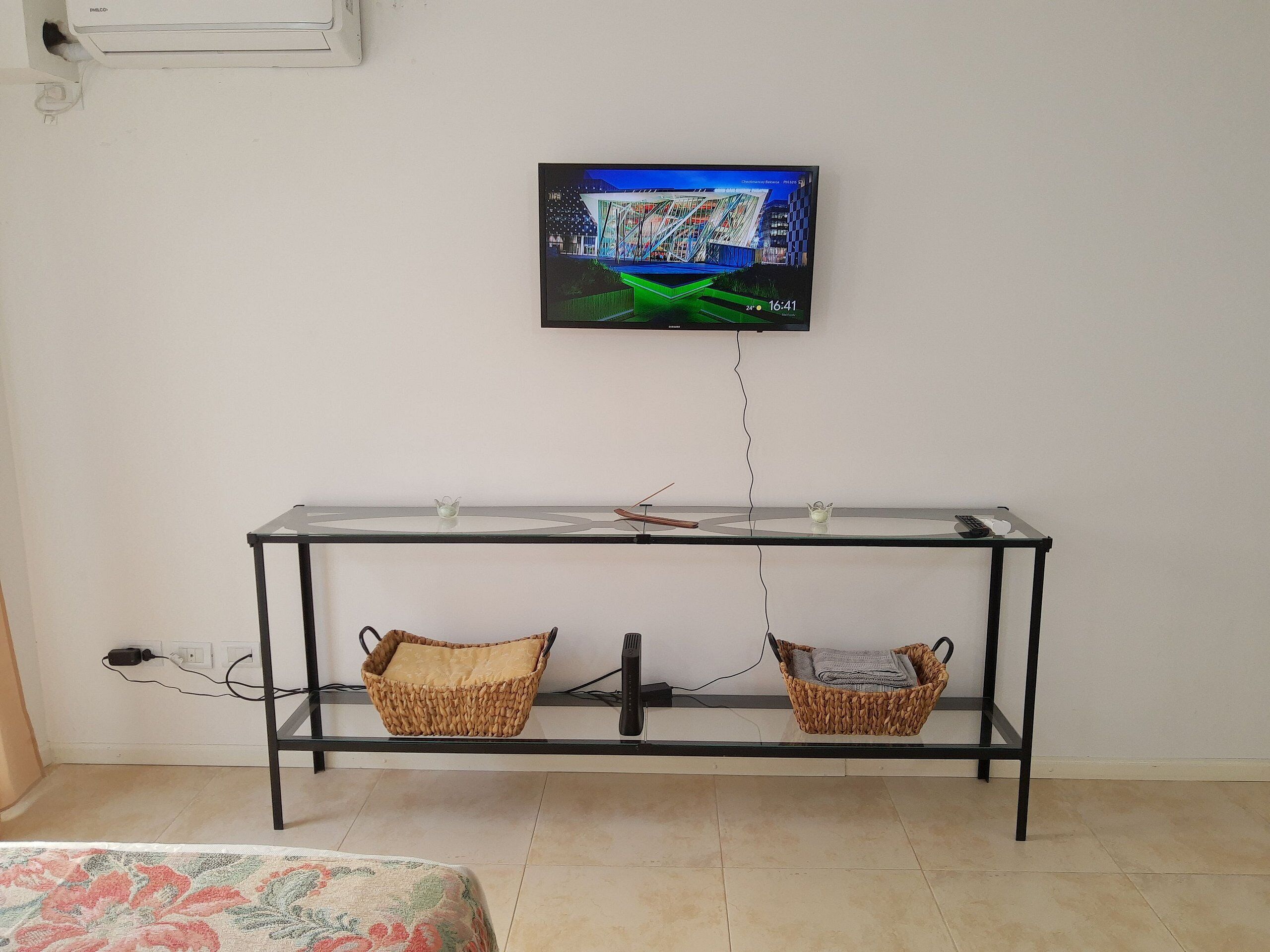 Ein modernes Wohnzimmer mit einem an der Wand befestigten Flachbildfernseher, einem Glastisch und zwei gewebten Körben, sowie einer Steckdose an der Wand.