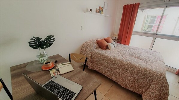 A bedroom with a bed, a desk with a laptop, a coffee cup, a notebook, and a plant. - Hornera Balcarce - Studio Apt Close to Everything (Rosario)