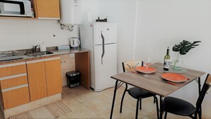 Una cocina compacta con microondas, refrigerador, lavamanos y un comedor con una mesa lista para dos.