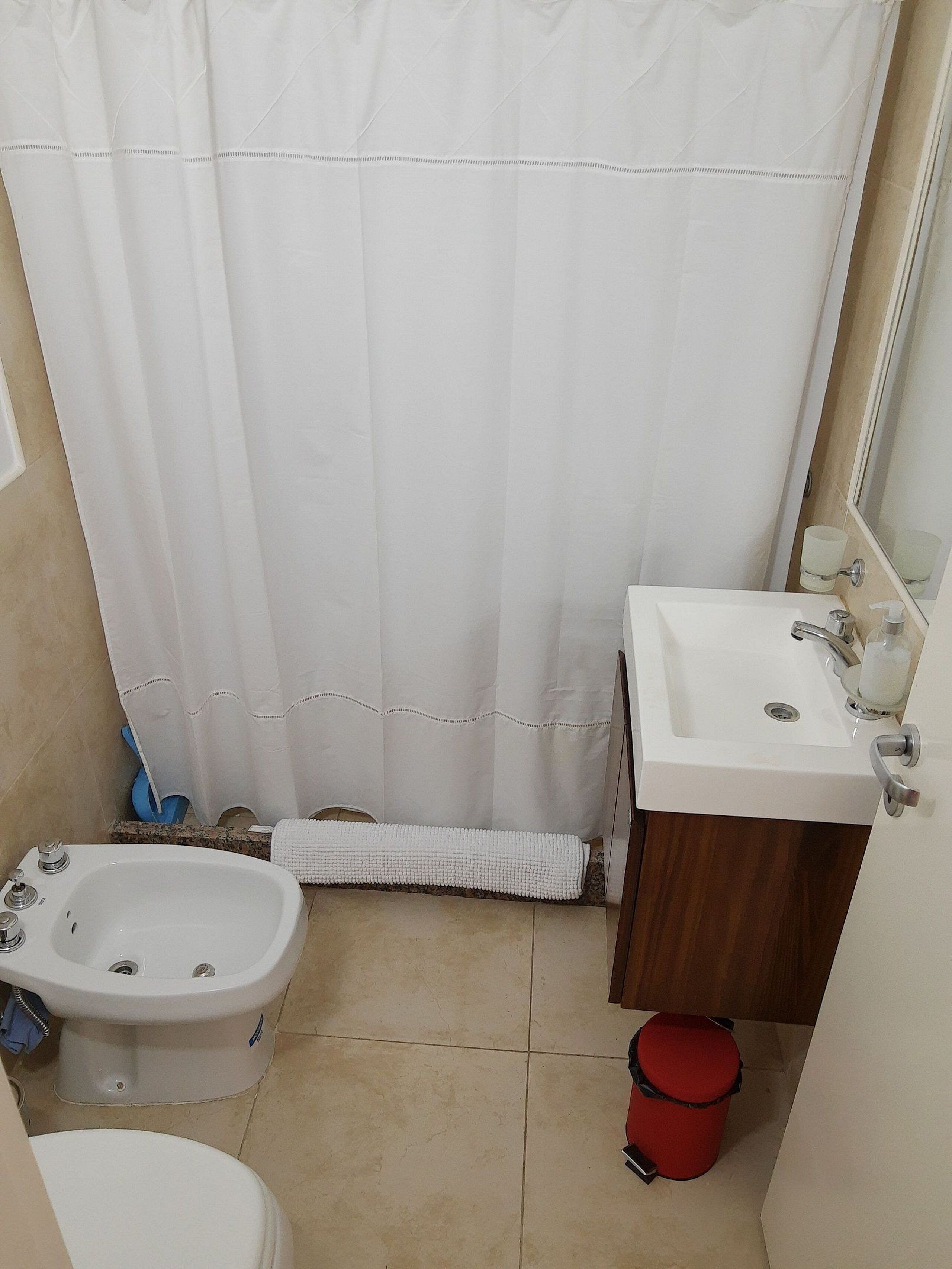 A small bathroom with a shower curtain, a sink, a bidet, and a toilet.