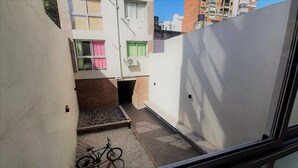Un estrecho callejón con una cama pequeña, una bicicleta y una ventana con cortinas rosadas.