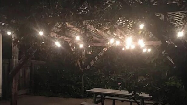 Un espacio al aire libre techado con luces colgantes, un banco de madera y una mesa de picnic.