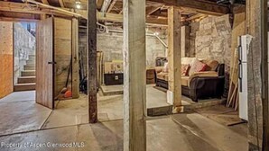 Un sótano rústico con vigas de madera a la vista, una pared de piedra, un sofá y un refrigerador.