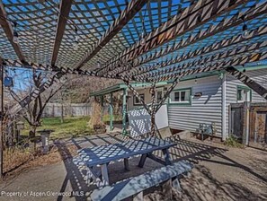 A covered patio area with a table and chairs, a pergola structure, and a house in the background. - An Oasis inside and out! Sweet cottage in Silt (Silt)