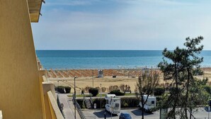 A view of a beach with a clear sky, a sandy area with orange barriers, and a parking lot with RVs and cars. - Lovely Flat in a Seafront Building (San Michele al Tagliamento)