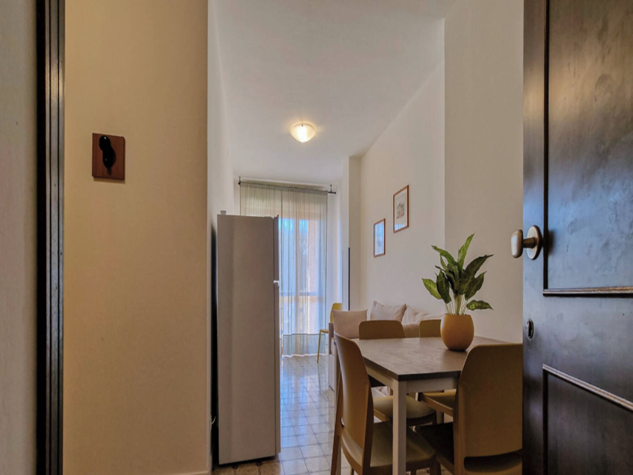 A compact kitchen with a refrigerator, a dining table with chairs, and a potted plant.
