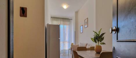 A compact kitchen with a refrigerator, a dining table with chairs, and a potted plant.