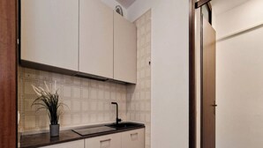 A compact kitchen with white cabinets, a black faucet, and a tiled backsplash. - Lovely Flat in a Seafront Building (San Michele al Tagliamento)