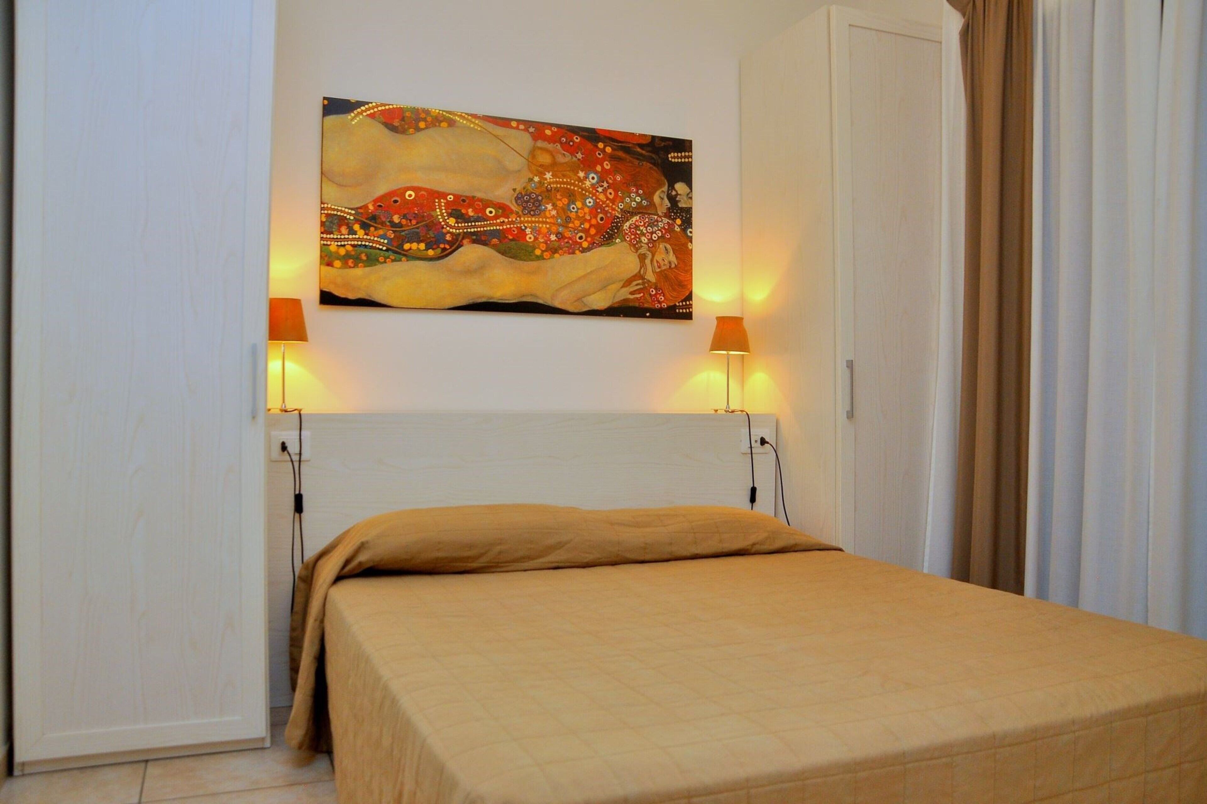 Een slaapkamer met een bed, een schilderij erboven en twee lampen aan weerszijden.