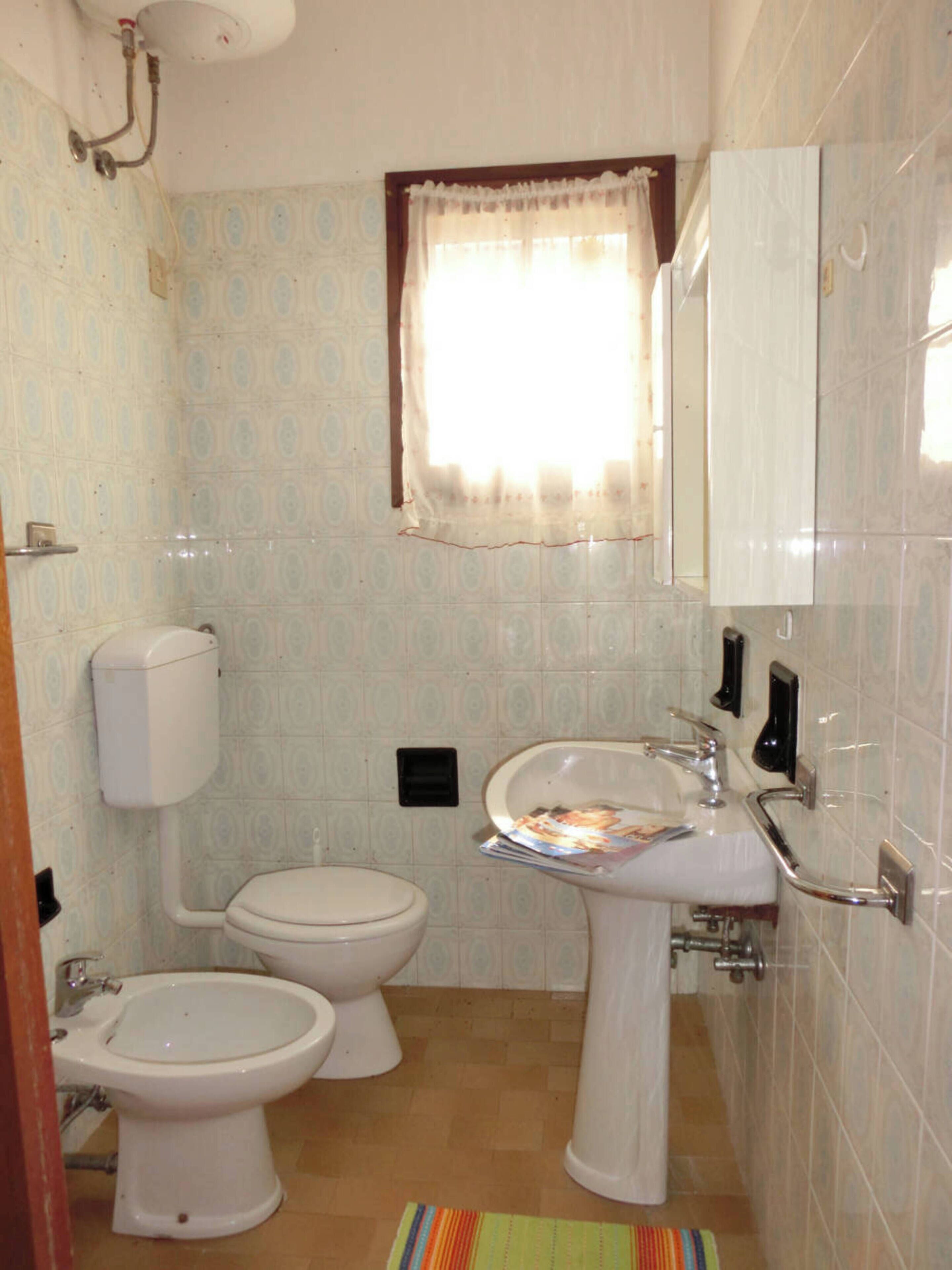 A bathroom with two toilets, a sink, a mirror, and a window with a curtain.