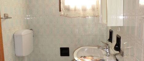 A bathroom with two toilets, a sink, a mirror, and a window with a curtain.