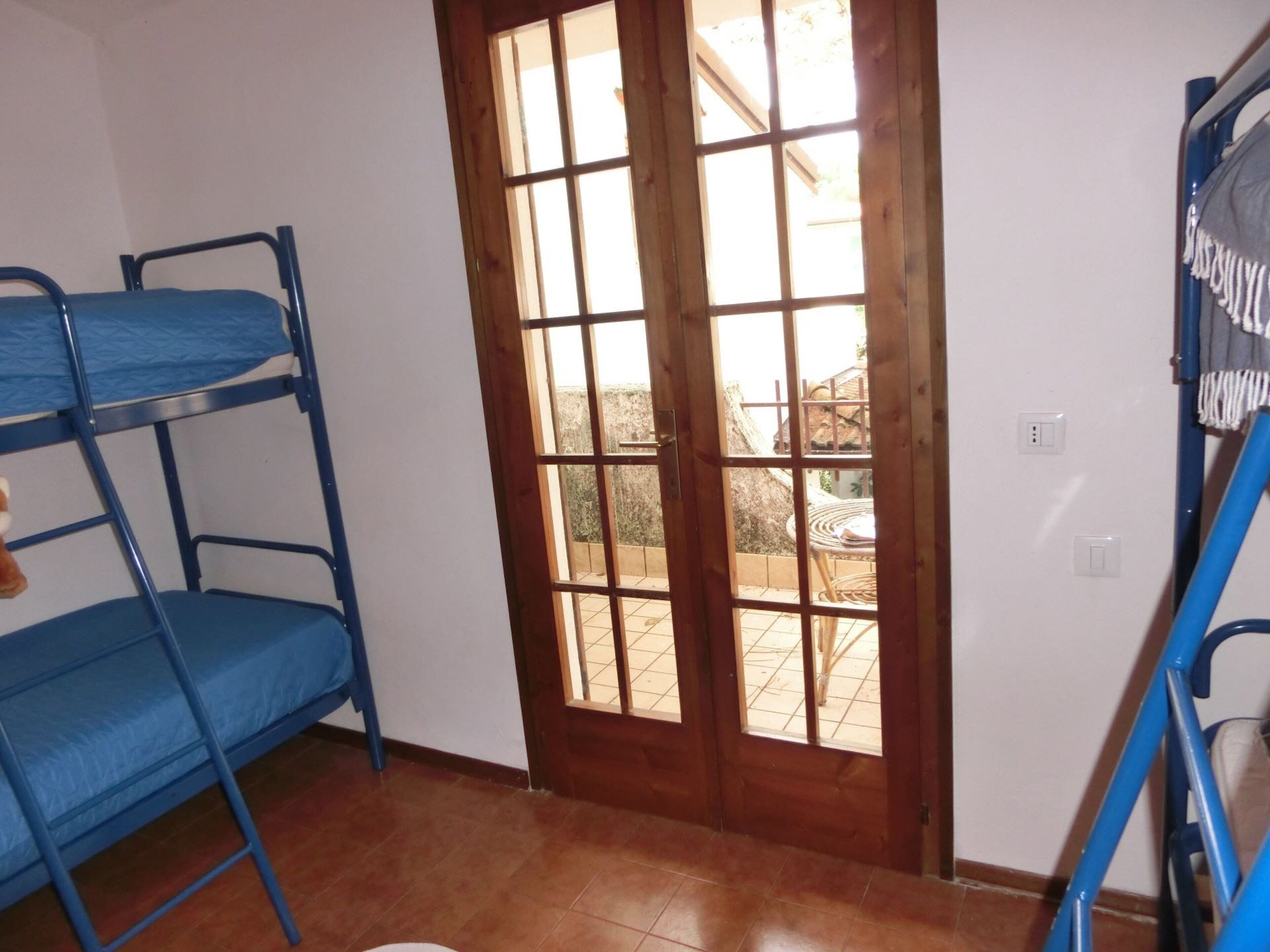 Une chambre avec des lits superposés, une porte en bois et une vue sur l’extérieur.