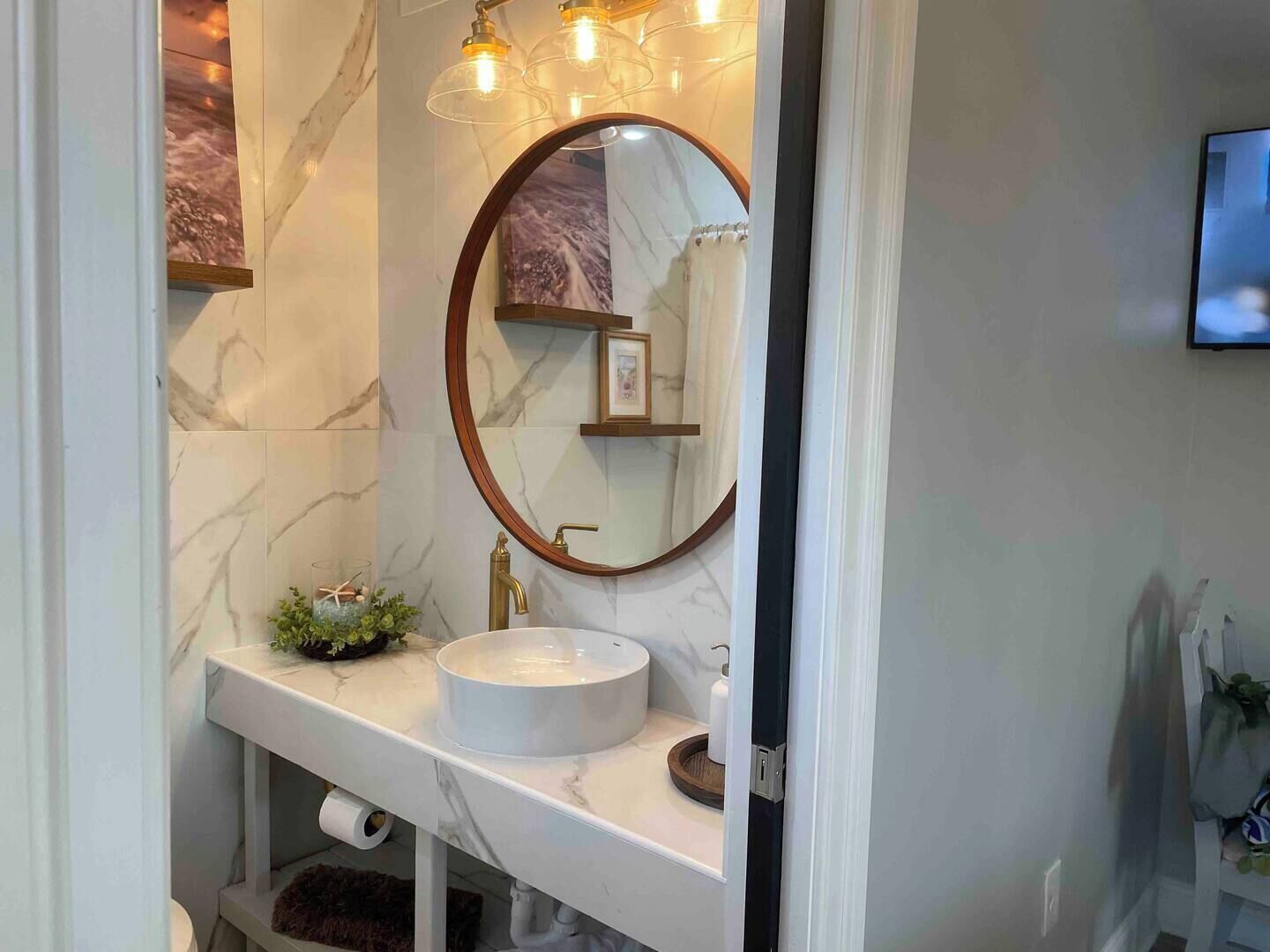 A bathroom with a marble sink, a round mirror with a wooden frame, and a wall-mounted light fixture.