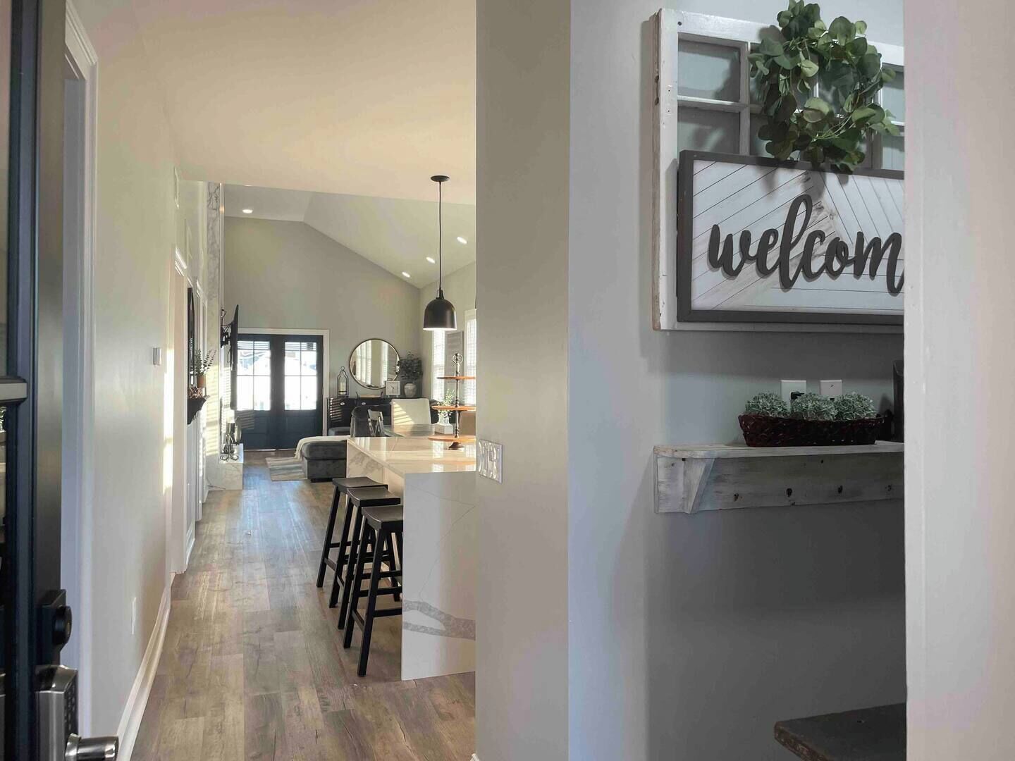 A modern kitchen with a bar area, a welcome sign, and a potted plant.