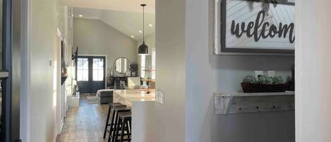 A modern kitchen with a bar area, a welcome sign, and a potted plant.