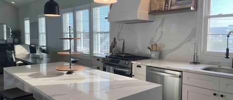 A modern kitchen with a large island, pendant lights, and a view of the city through large windows.