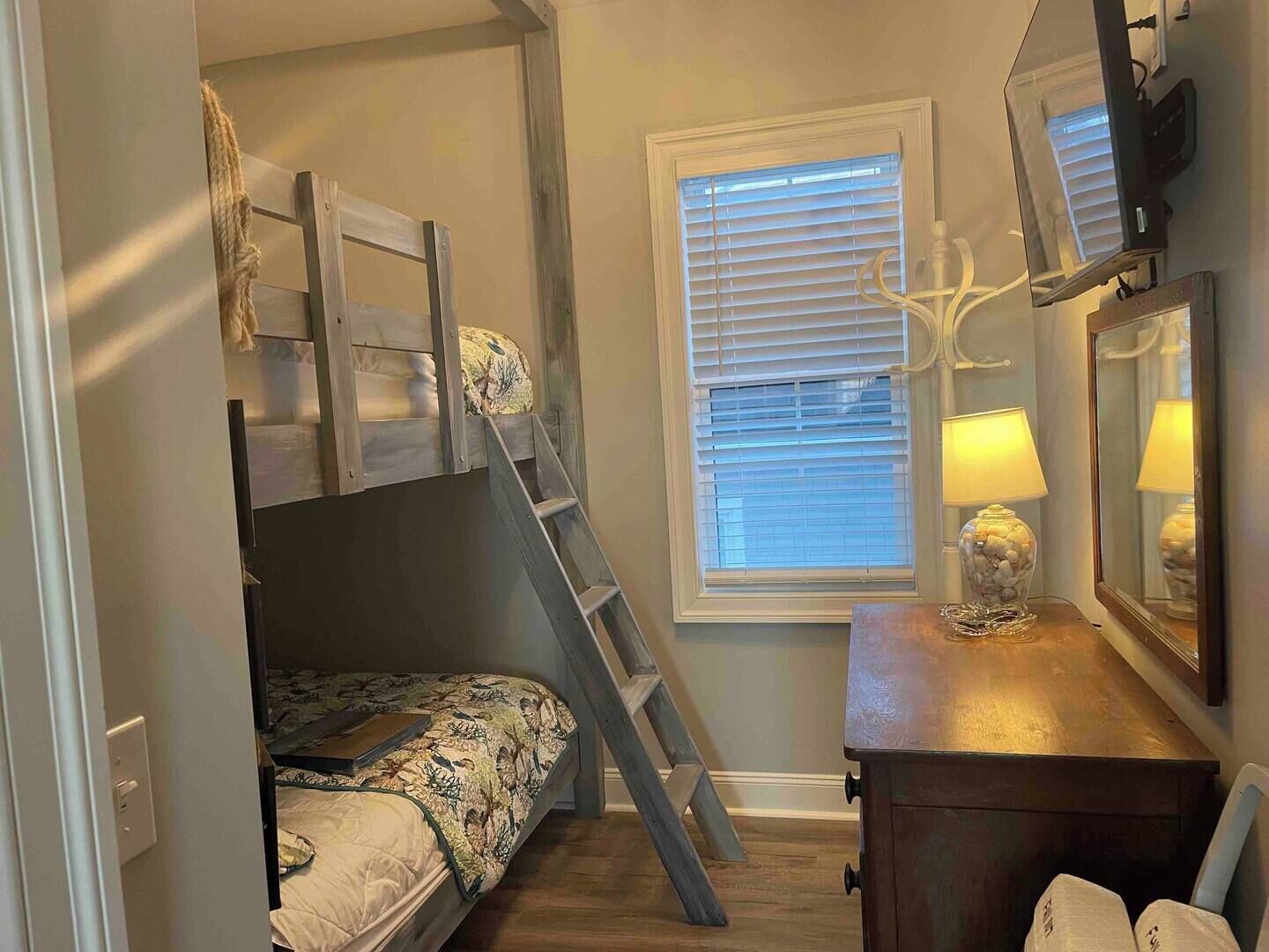 A bedroom with a bunk bed, a ladder, a bedside table with a lamp, and a window with blinds.