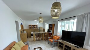 A modern living room with a sofa, a coffee table, a TV, and a kitchen area with a dining table and chairs. - Modern Beach Retreat with Pool- 5-Min Walk to Punta Hermosa’s Best Beach (San Miguel)
