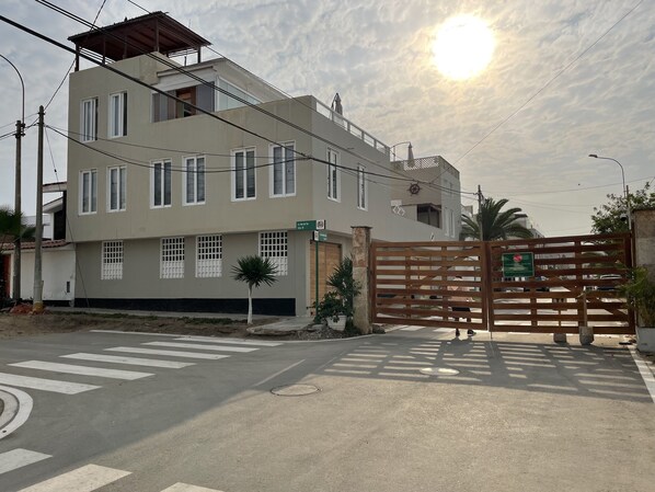 Un edificio residencial de varios pisos con un acceso con puerta, un paso de peatones y una calle con vehículos.