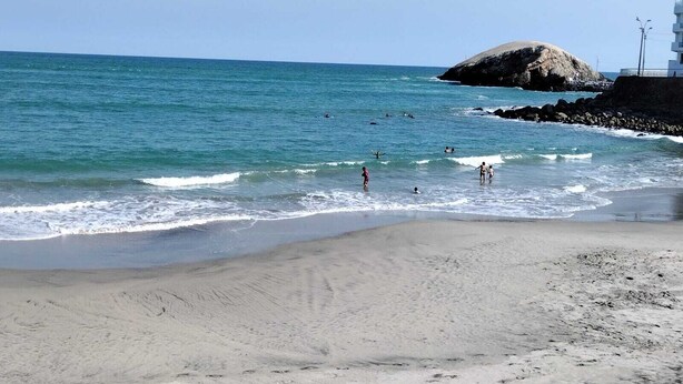 A beach with clear blue water, rocky outcrops, and a few people swimming and walking along the shore. - Modern Beach Retreat with Pool- 5-Min Walk to Punta Hermosa’s Best Beach (San Miguel)