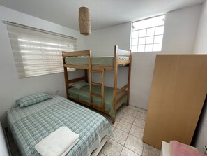 Una habitación con literas, una cama individual, una ventana con persianas y una lámpara colgante.