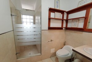 Un baño con cabina de ducha de vidrio, inodoro y lavamanos.