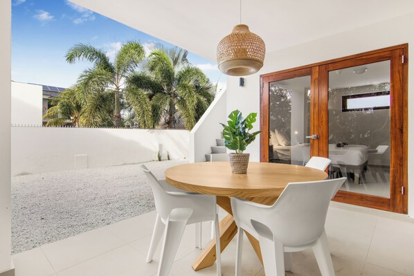 A round wooden table with white chairs, a hanging woven light fixture, and a potted plant.