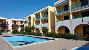 A hotel with multiple balconies, a swimming pool, and a clear sky.